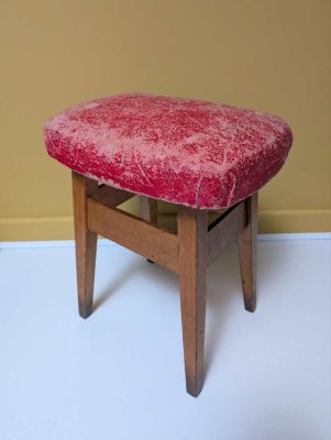 Vintage beech stool with worn, red cushioned seat